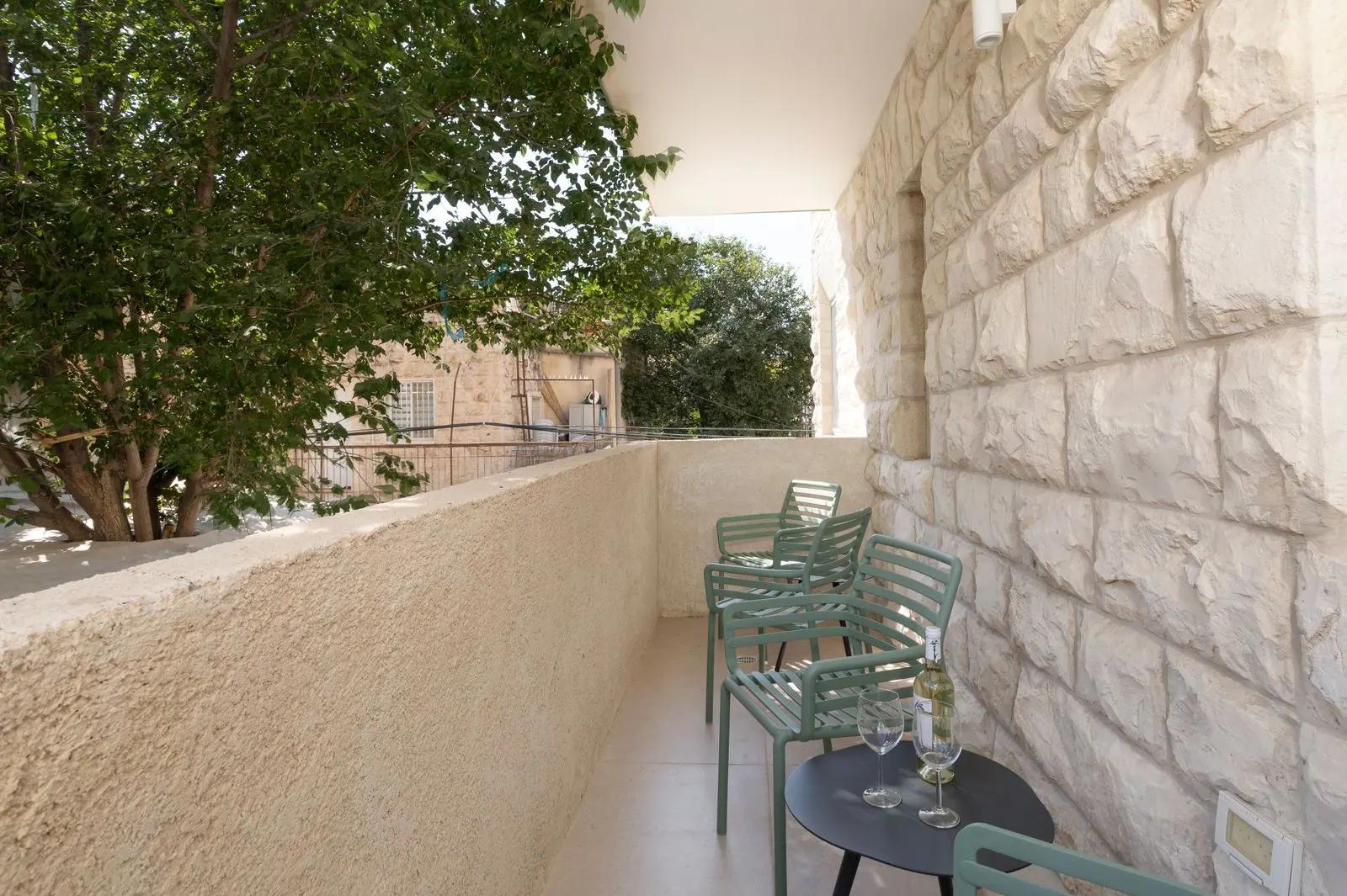 מרפסת בדירה 7 — קיר אבן ירושלמית וכיסאות ירוקים